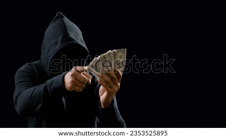 Hands of a man wearing a black shirt, sitting on a chair and a table, is a thief, holding money, counting the amount obtained from hijacking or robbing, in a dark background
