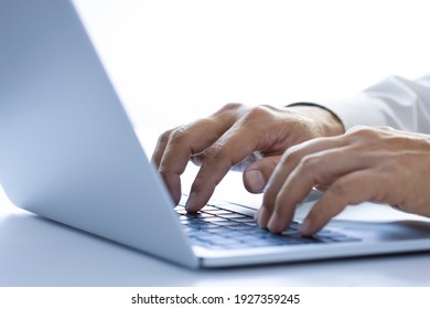 Hands of a man with white shirt typing on a laptop or notebook computer on a desktop while working in the office using internet, input data for information analysis and sending an email message.