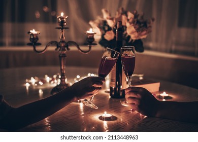 Hands man and woman holding glasses of wine having romantic candlelight dinner at table at home. Hands man and woman holding glass of wine. Concept of Valentine's day or Candlelight date at night. - Shutterstock ID 2113448963