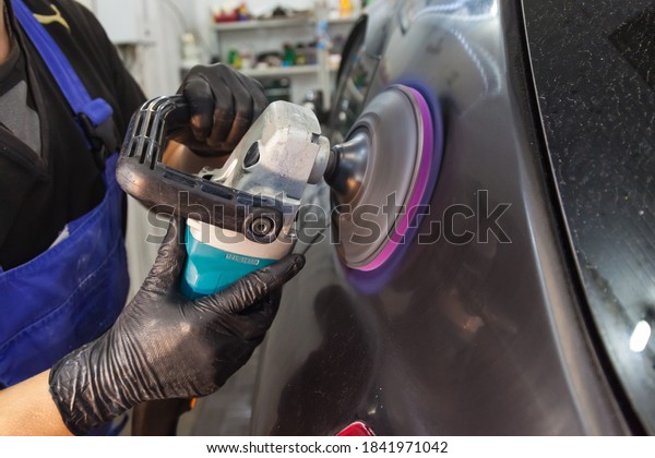 The hands of a master in a car service with\
gloves hold a polishing machine and use this tool to polish the\
body of a black car with a special wax to protect it from minor\
scratches and damages.