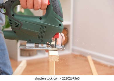 The hands of a master carpenter with an electric jigsaw in his hands cutting off a piece of wood. Male hands using fret saw for cutting wood. A carpenter cuts wood with a jigsaw in a home workshop.