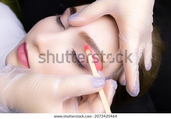 the hands of the master white gloves\
stretch the eyebrow of the model apply wax to remove unwanted hairs\
after the procedure of coloring and\
lamination