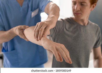 Hands Of Mature Clinician In Blue Uniform Supporting Bent Arm Of Young Patient During Physiotherapeutic Training In Rehabilitation Clinics