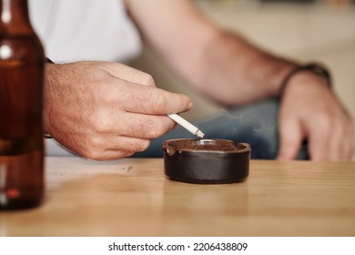 Hands Of Mature Man Shaking Off Ashes In Ashtray On Table