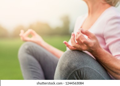 Hands of mature woman practicing yoga at lotus pose, outdoors