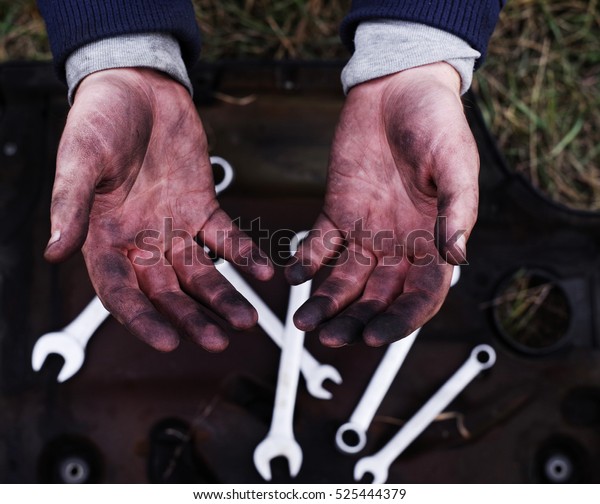 Hands of a mechanic in oil and fuel\
oil against the background of wrenches, close\
up