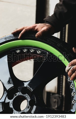 Hands of a mechanic on top of a wheel of a green super sports car.