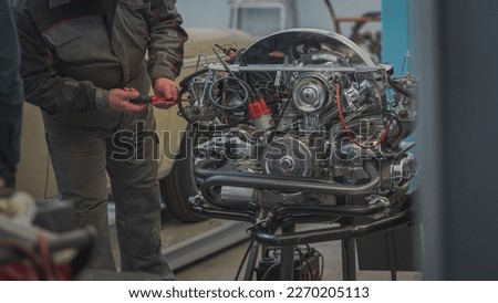 Hands of a mechanic are visible adjusting or setting idle or air mixture screws on a vintage freshly rebuilt air cooled engine. Carburetor setting with running engine on testing stand