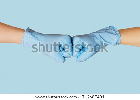 Hands in medical gloves greeting each other with fist bump on blue background.