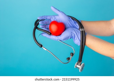 Hands in medical gloves holding a red heart shape model on blue background. Cardiology, organ donation or Healthy heart concept.