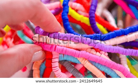 Hands meticulously organize a kaleidoscope of multicolored, patterned clay beads, intricately coiled and laid out against a stark white backdrop.