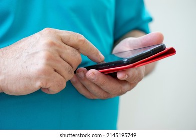 Hands Of A Middle-aged Man In A Blue T-shirt With A Smart Phone With A Red Case