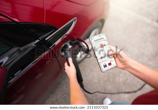 Hands with a mobile phone and\
charging plug on the background of a carsharing electric\
car