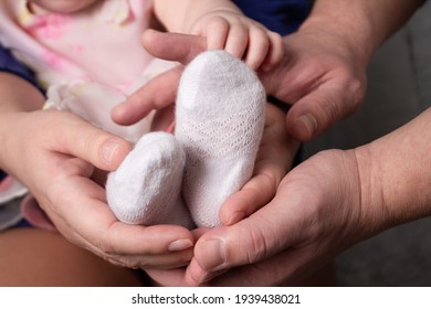 The Hands Of Mom And Dad Hold The Baby's Baby Legs