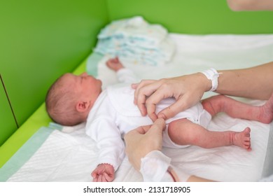 Hands Of A Mom Who Just Gave Birth In The Maternity Hospital With The Hospital Identification Bracelet And The Medication Line Puts A Bodysuit On Her Newborn Baby After Changing Her Diaper