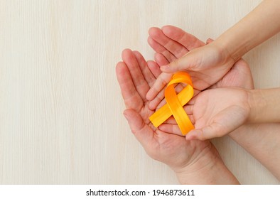 Hands Of Mother And Child Hold Orange Ribbon On White Background.Concept. World Multiple Sclerosis Day.Leukemia Cancer Awareness. COPD And ADHD. Layout. Copy Space. Banner. Mock Up.close Up