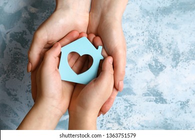 Hands Of Mother And Child With Model Of House On Color Background. Concept Of Earthquake