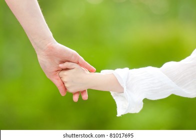 Hands Of Mother And Daughter Holding Each Other. Summer Park In Background