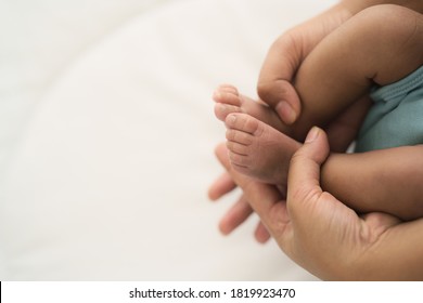 Hands Of Mother Grabbing Infant Baby Feet While Holding