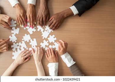 Hands of multi-ethnic team assembling jigsaw puzzle, multiracial group of black and white people joining pieces at desk, successful teamwork concept, help and support in business, close up top view - Shutterstock ID 1022439421