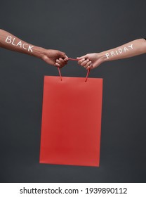 Hands Of Multiracial Man And Woman With Black Friday Inscription Holding Red Packet Mockup On Dark Background, Vertical Shot. Discount And Sale Concept