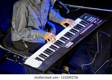 Hands of musician playing an electronic keyboard on stage with blue lighting. - Shutterstock ID 1153392736