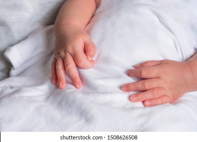 Hands Of Newborn Showing OK Gesture In Sign Language On White Cloth. Close-up Of Baby Hands. Family Concept