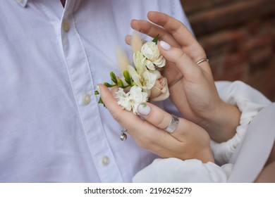 The hands of the newlyweds with gold rings close-up against the background of a plaid jacket with a boutonniere.