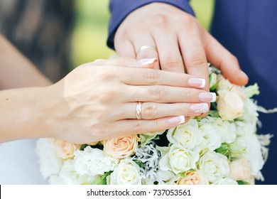 hands of newlyweds with wedding rings on a wedding bouquet