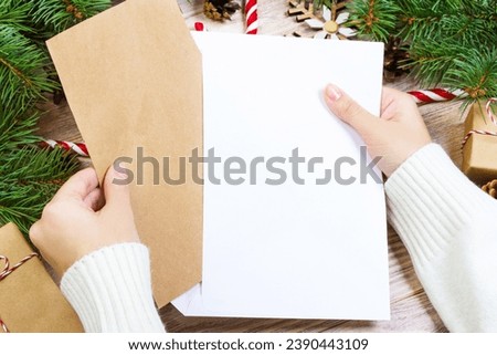 Hands with notebook and an envelop for letter. A girl is ready to send a letter with wishes to Santa Claus.