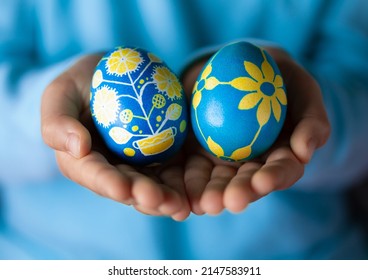 Hands of obscured girl holding Easter eggs painted with Ukrainian national colors, blue and yellow, and depicting Ukrainian ornaments