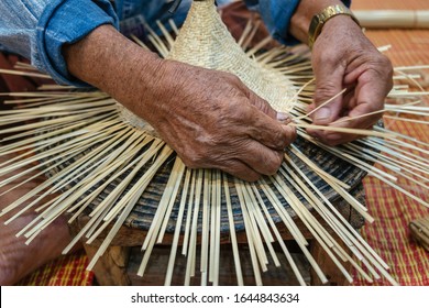 Hands of old artisan craftsman elderly working weaving rattan and bamboo to make ancient handmade handcraft wicker traditional Thai wooden hat