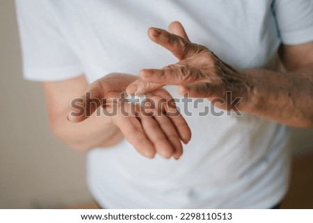 Hands of old elderly applying lotion on hands, rubbing her palm with thumbs cream. Prevent dryness, nourishing dry skin and care for sensitive skin.