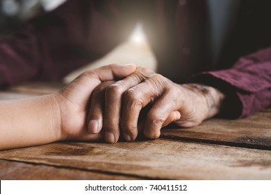Hands of the old man and a child's hand on the wood table
