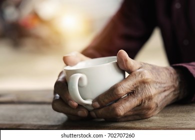 Hands of old man holding cup of coffee on the wood table.vintage tone