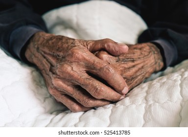 Hands of an old man with wrinkled and wrinkles on a white bed in a hospital.