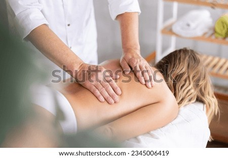 Hands of old masseur conducting back massage for woman client in procedure room