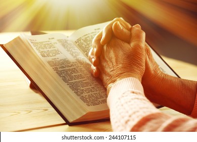 Hands of old woman with Bible on table and dark background - Powered by Shutterstock