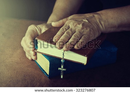Hands of old woman with Bible on table.
