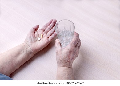 The Hands Of An Old Woman With A Glass Of Water And Pills. Timely Taking Of Medications During Home Therapy