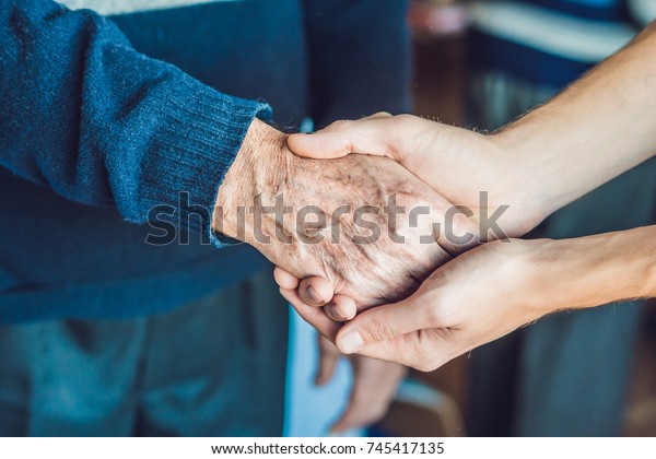 Hands of an old woman and a young man. Caring for the\
elderly. close up.