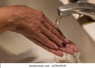 Hands Of An Older Woman With Painted Nails On Water Running From A Tap. She Is Washing Her Hands.