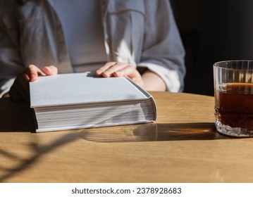 Hands on abstract book. Reader in cafe at wooden table with coffee glass