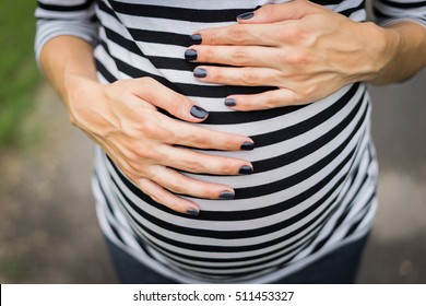 Hands On The Belly Of The Pregnant Woman, The Last Month Of Pregnancy, The Gentle Touch Of The Abdomen, Nail Polish On Hand, Black Lacquer Stripes Shirt.