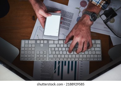 Hands on a computer keyboard and typing on a phone in an office with paper work from above. Closeup of a business man browsing the internet, finishing a report or sending a communication email - Shutterstock ID 2188929585