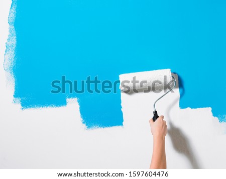 Hands on rollers and paints blue walls white
