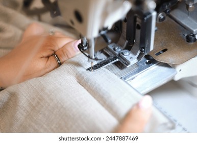 Hands on a sewing machine working in a textile factory industrial setting. Metal cotton sewing machine industry. Cotton sewing and fabrication textile industries. Metal hanger rails. - Powered by Shutterstock