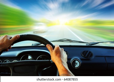 Hands On Steering Wheel Of A Car Driving On An Asphalt Blurred Road