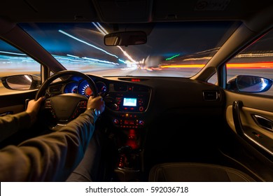 hands on the wheel a car moves at fast speed at the night. Blured road with lights with car on high speed. Car speed night drive on the road in city