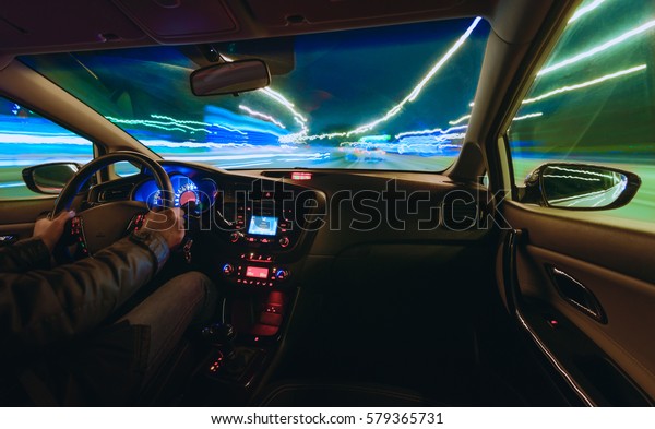 hands on the\
wheel a car moves at fast speed at the whinter night. Blured road\
with lights with car on high\
speed